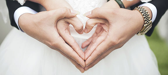 A man in a tuxedo and a woman in wedding dress making a heart with their hands.God intended traditional relationships.